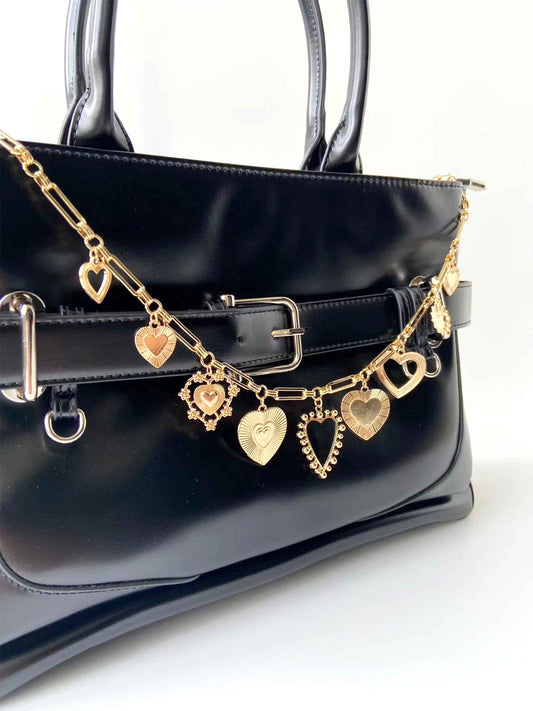 Golden heart pendant chain adorns black bag, eye - catching and stylish.
