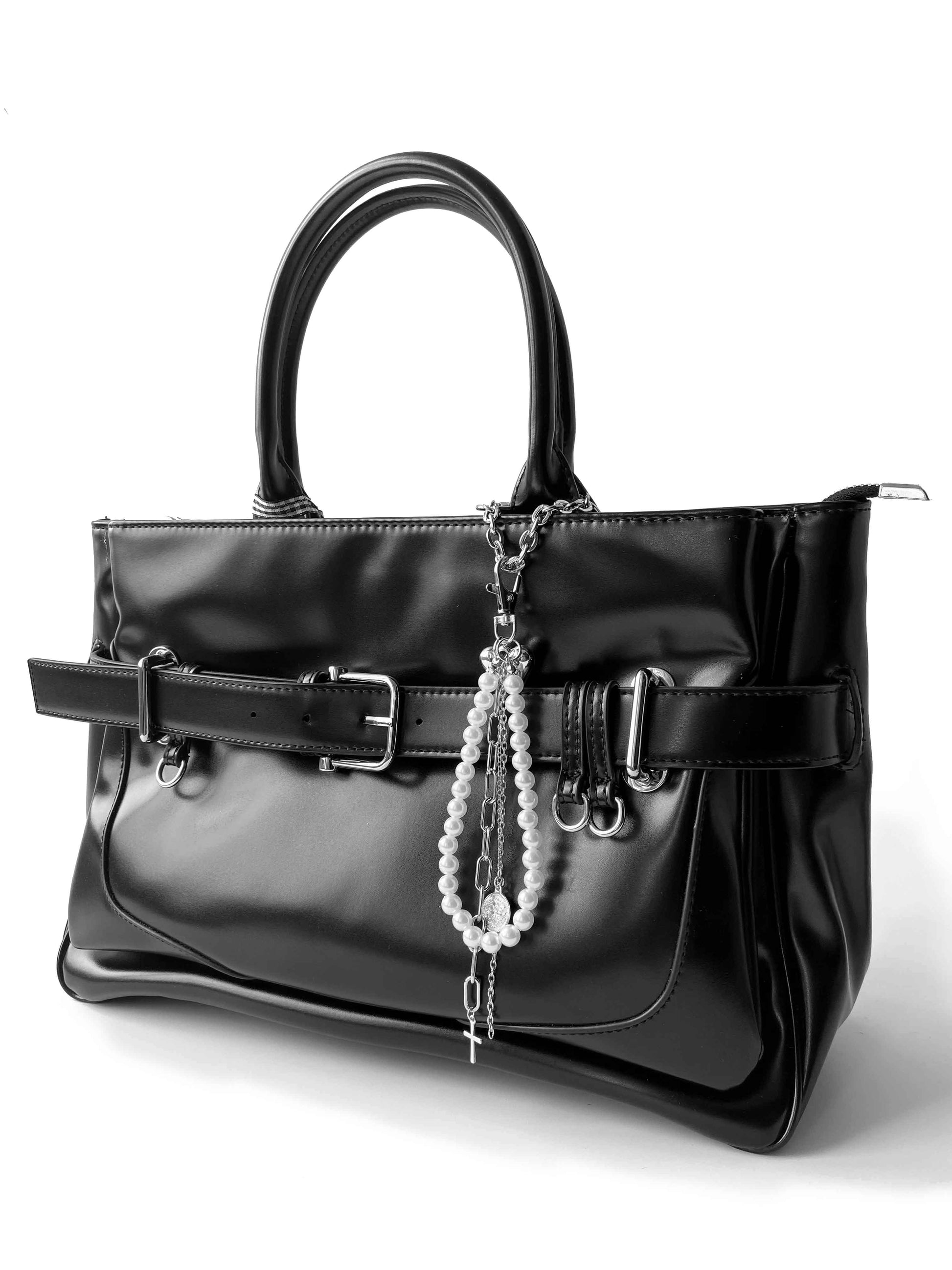 Black leather handbag with wide belt, decorated with faux pearl cross charm, showcasing edgy punk style.