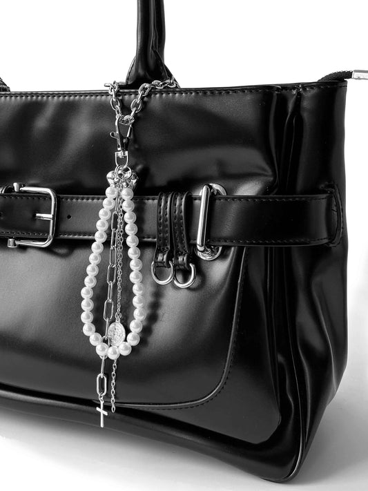 Punk-style multi-layer charm, faux pearl chain with cross and metal coin, on glossy black leather bag.