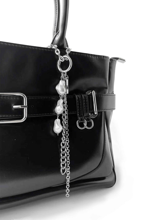 Close-up of handbag details showcasing textured leather and exquisite metal buckle, with dangling pearl chain for elegance.