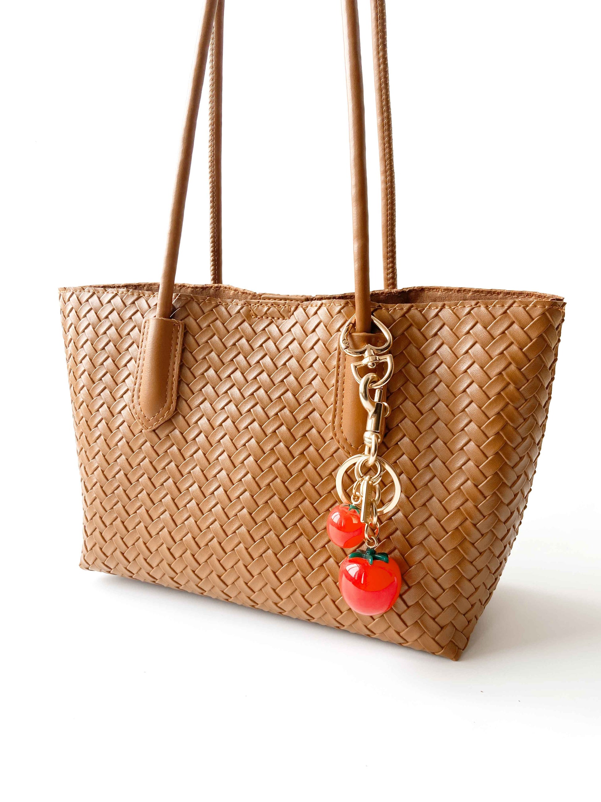 Tomato bag charm adorns the woven tote bag, stylish and eye - catching