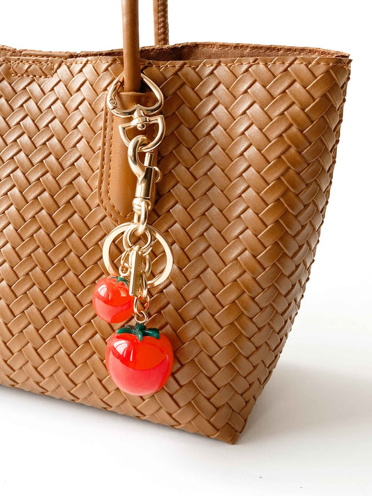 Tomato - shaped bag charm adds lively color to the brown woven bag.