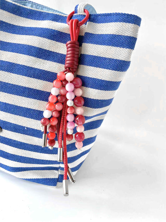 Pink - red beaded leather tassel charm adorns the blue - white striped bag, stylish and eye - catching.