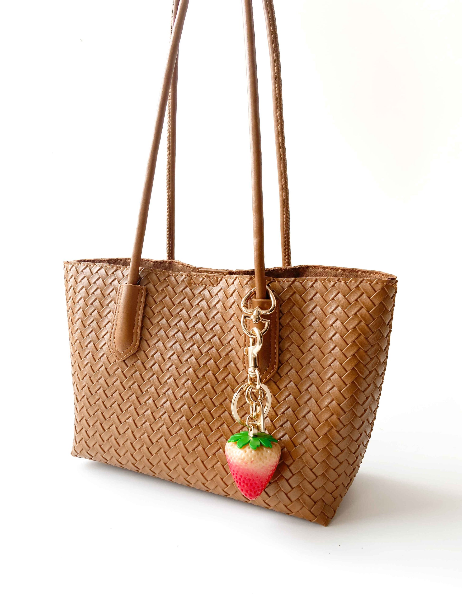 Strawberry bag charm adorns the woven tote bag, stylish and playful.